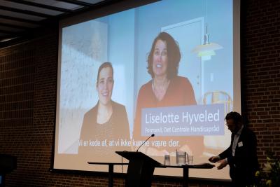 Billedet viser Det Centrale Handicapråds formand, Liselotte Hyveled, hilse på deltagerne i en videohilsen sammen med social- og indenrigsminister Astrid Krag.