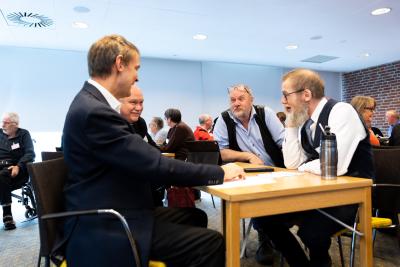 Tre mænd taler sammen under en workshop.