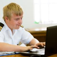 Ung mandlig pilot med down syndrome arbejder ved sin computer
