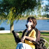 Kvinde i kørestol med mundbind om sommeren ved en sø