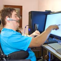 Ung mand med handicap sidder i sin kørestol og arbejder hjemmefra ved computer. 