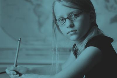 Pige med briller sidder foran verdens-kort. Hun har en blyant i hånden.