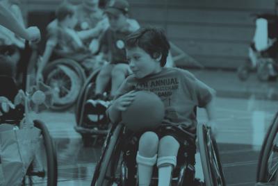 Dreng spiller bold i en idrætshal. Han bruger kørestol. Det gør de andre spillere også.